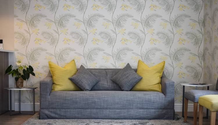 ujęcie wnętrza domu z szarą kanapą i ścianą z tapetą ze wzorami liści